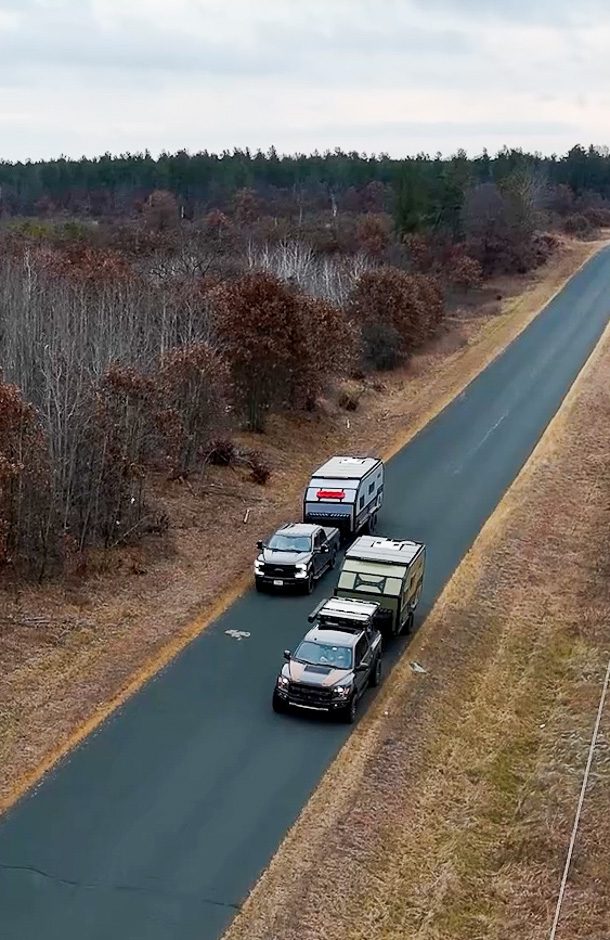Two Imperial Outdoor Xplore Series campers being pulled on a narrow country road.