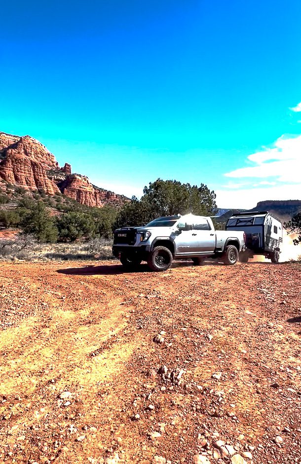 a GMC AT4X AEV truck pulling up the Imperial Outdoors X195 on a steep trail causing dust to fly up.