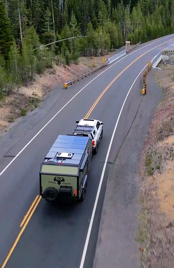 Imperial Outdoors X195 off grid trailer traveling along a quiet highway in the pine forest.