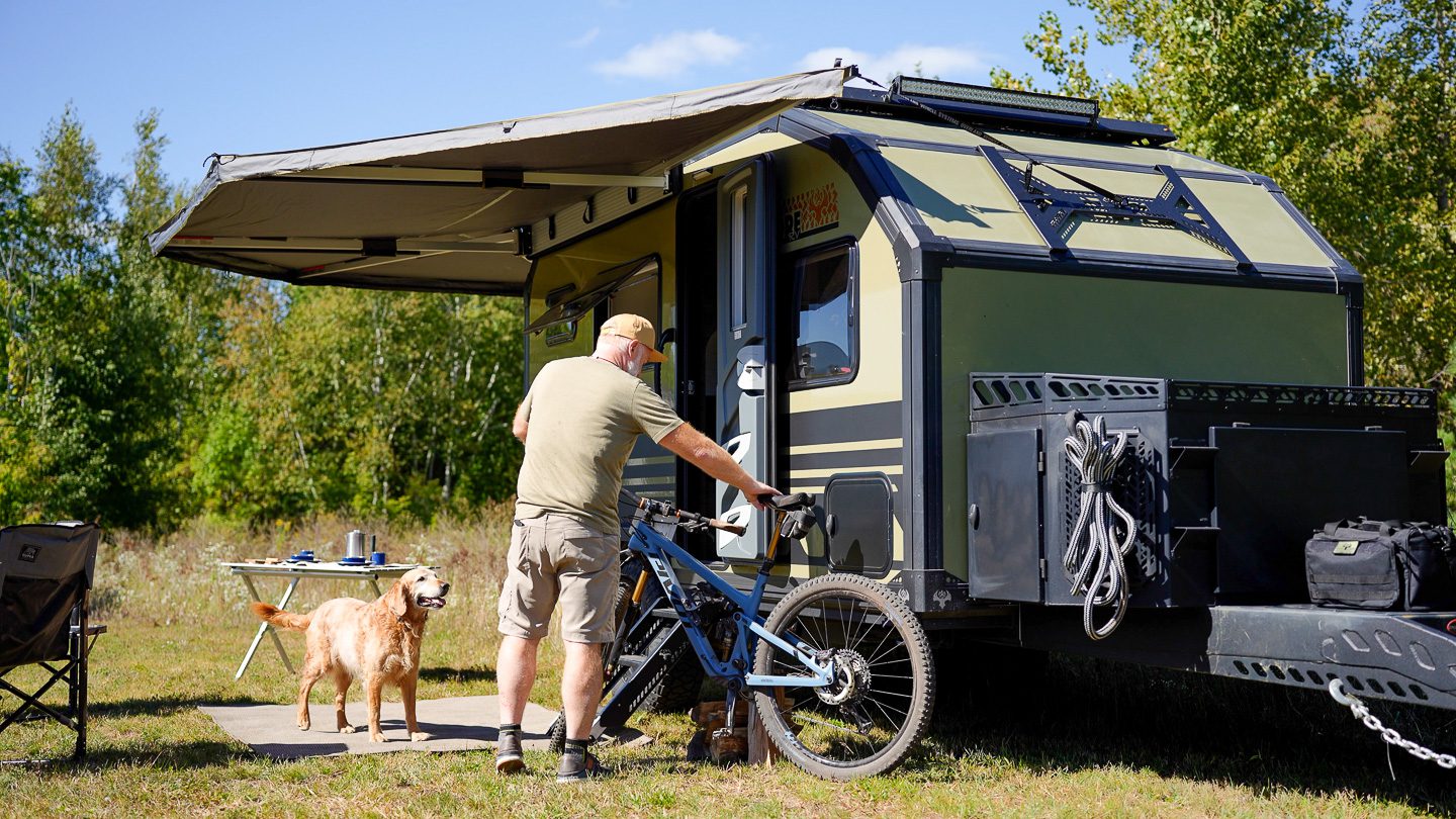 Imperial Outdoors Xplore Series X145 camper man mountain biking with his golden retriever.