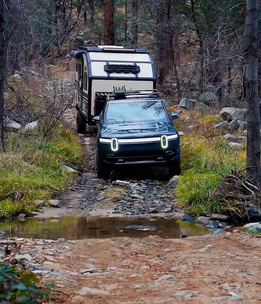 Tight narrow trail with a Rivian pulling a X145 from Imperial Outdoors about to cross over a creek passing.