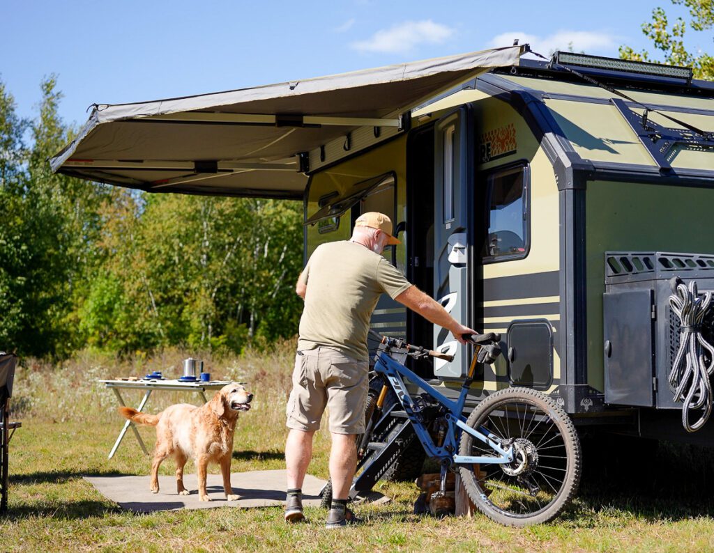 Base off grid camp in the mountains of Montana, man getting ready to go mountain biking while camping with his golden retriever.