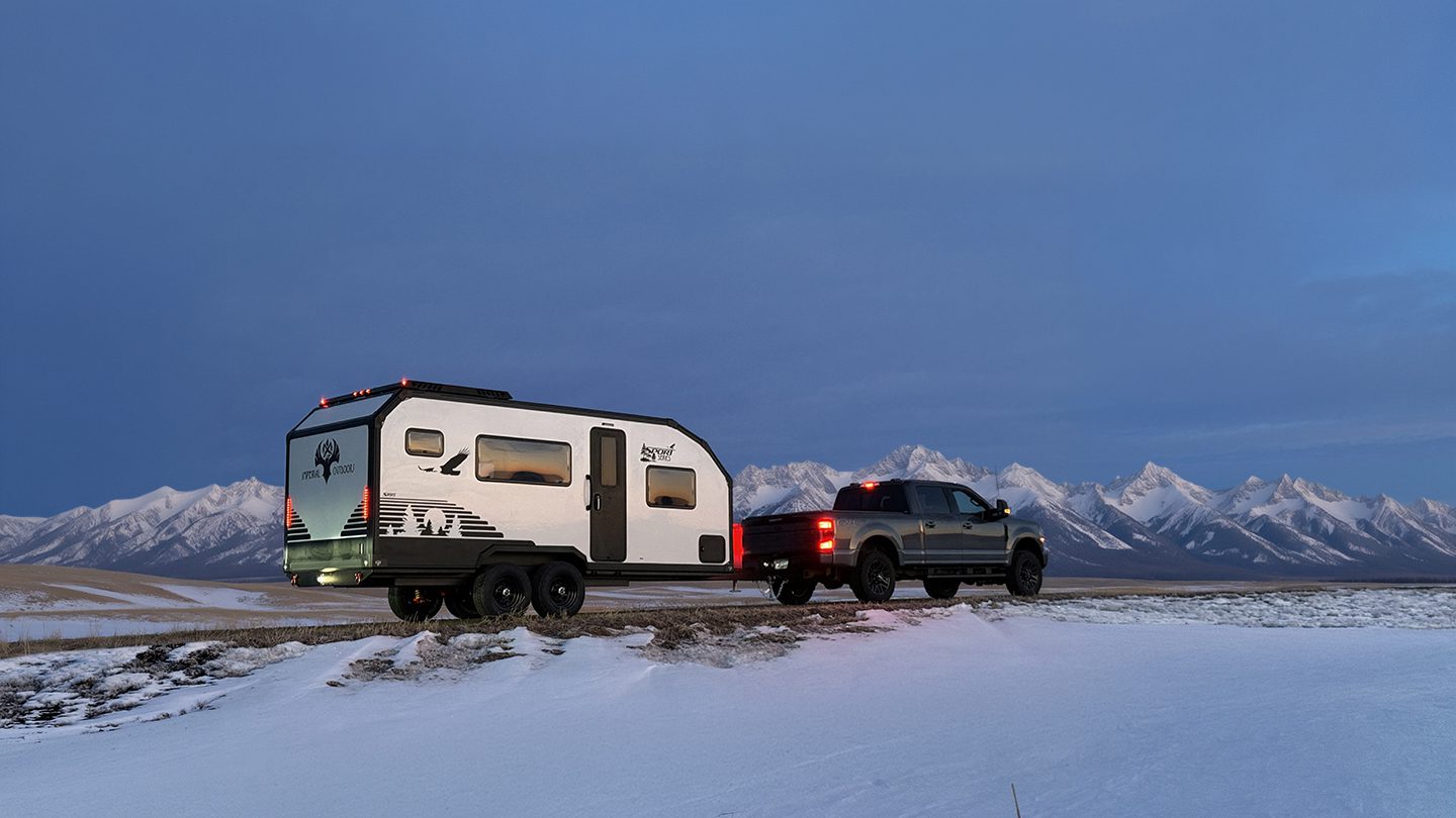 Imperial Outdoors S195 traveling on an off beaten snowy road with the Rocky Mountains in the background.